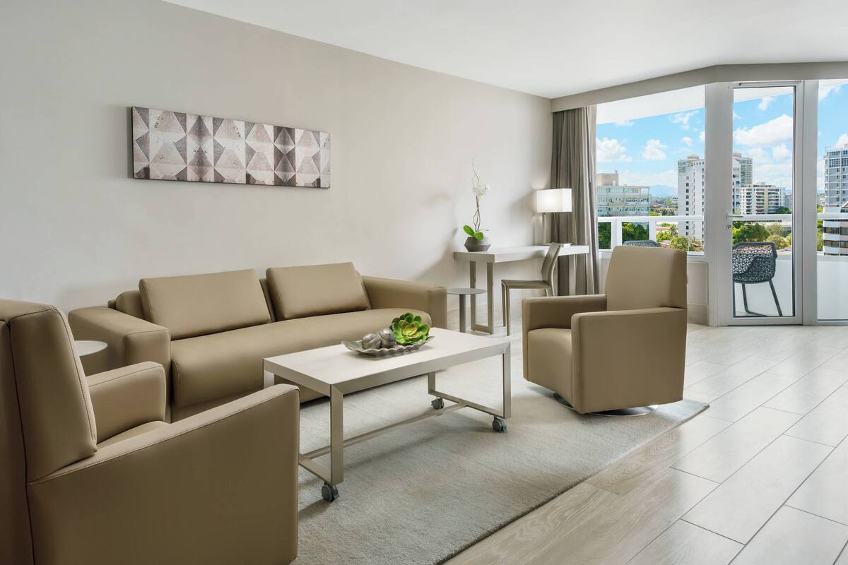 Ein modernes Wohnzimmer mit einer Couch, Sesseln, einem Couchtisch und Blick auf die Stadt durch große Fenster.