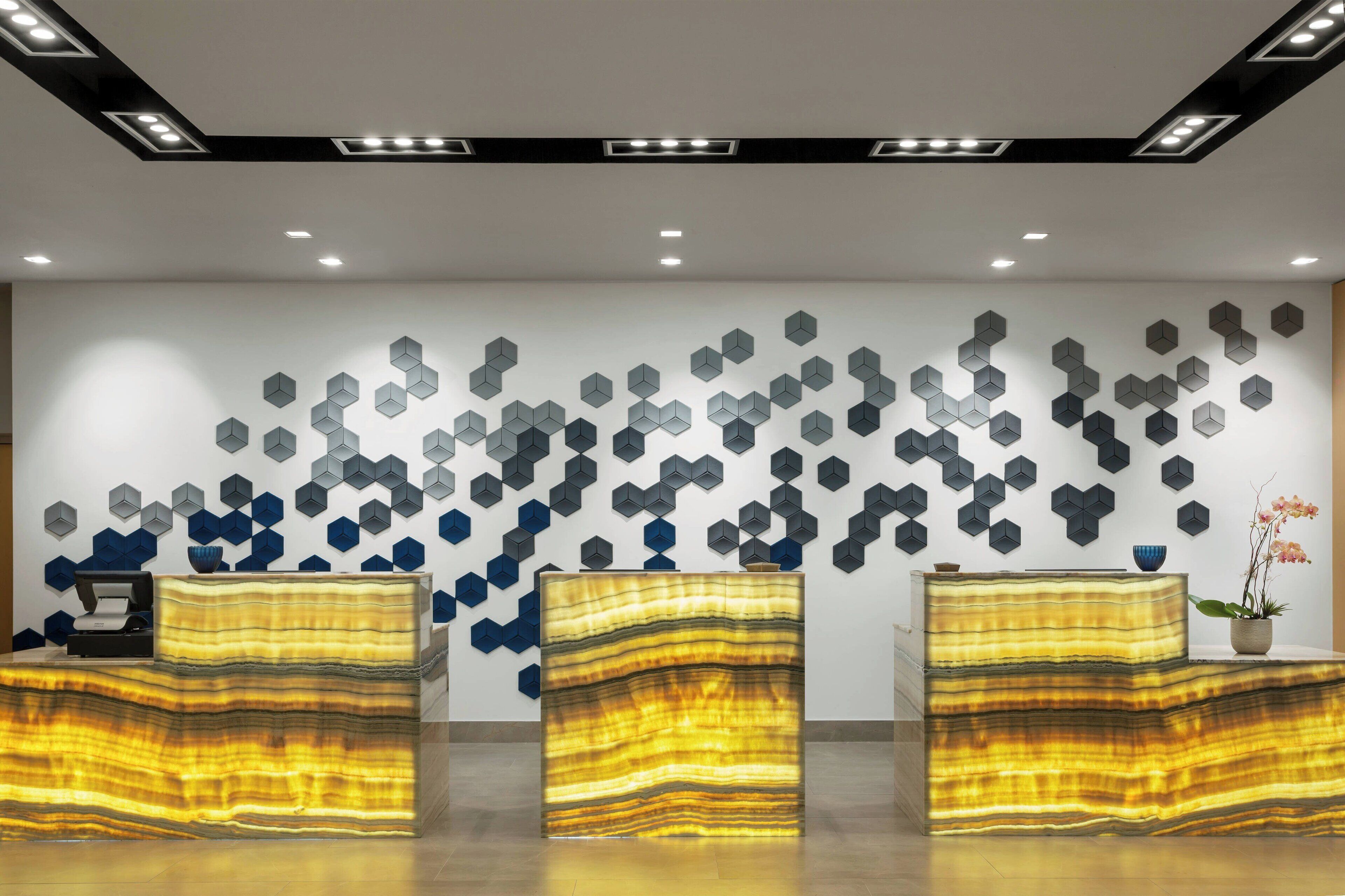 A reception area with a modern design, featuring a patterned wall and three reception desks with a unique layered design.
