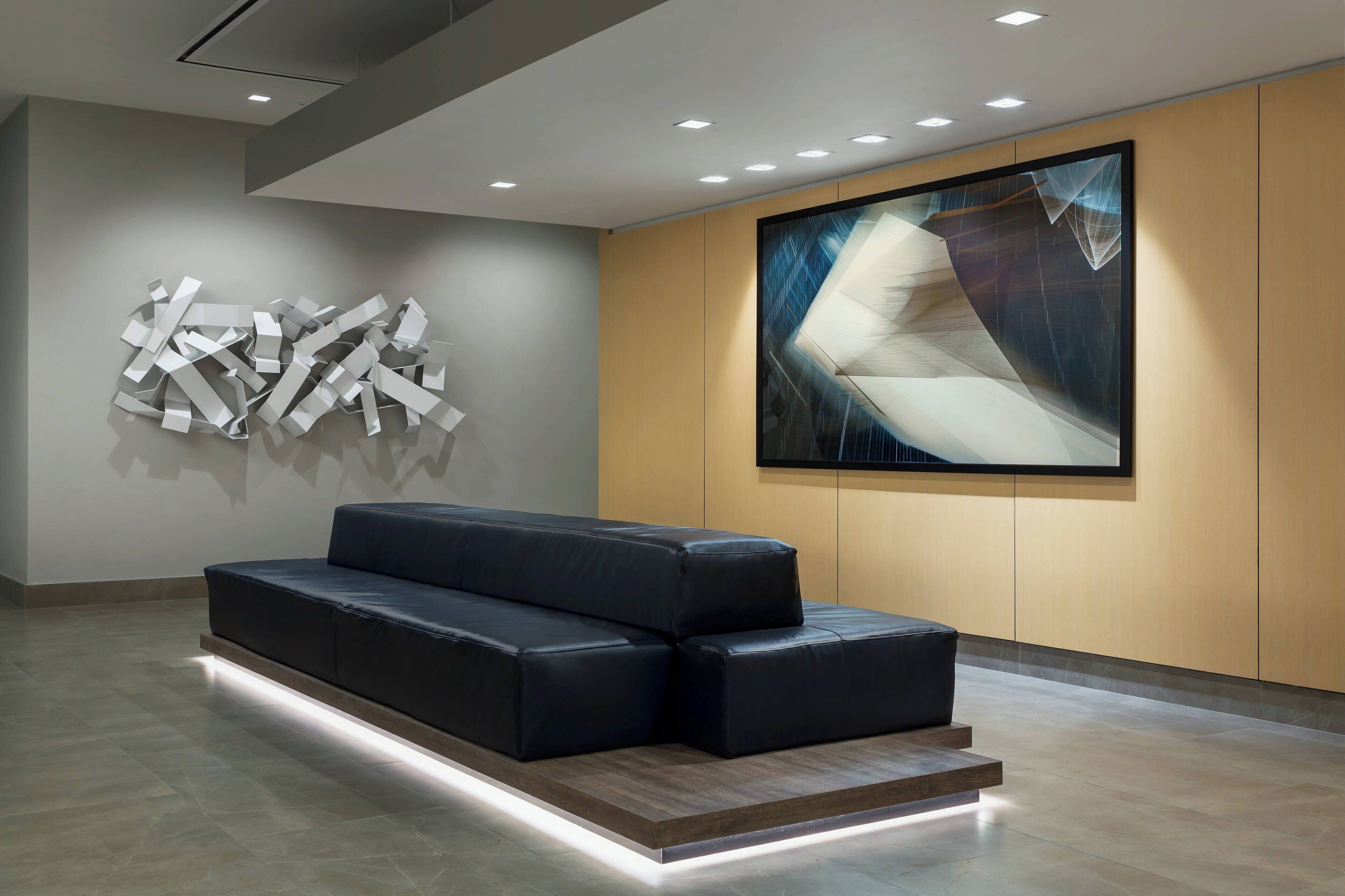 A modern lobby with a black leather sofa, abstract wall art, and recessed lighting.