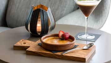 A dessert dish with a strawberry on top, a martini glass with a garnish, and a candle in a decorative holder on a round table.