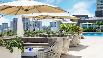 A rooftop lounge with outdoor seating, umbrellas, and a pool.
