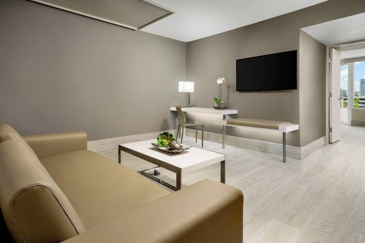 Ein modernes Wohnzimmer mit Sofa, Couchtisch, Fernseher und Essbereich mit Lampe und Pflanze.