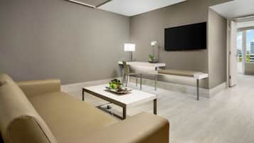 A modern living room with a sofa, a coffee table, a TV, and a dining area with a lamp and a plant.