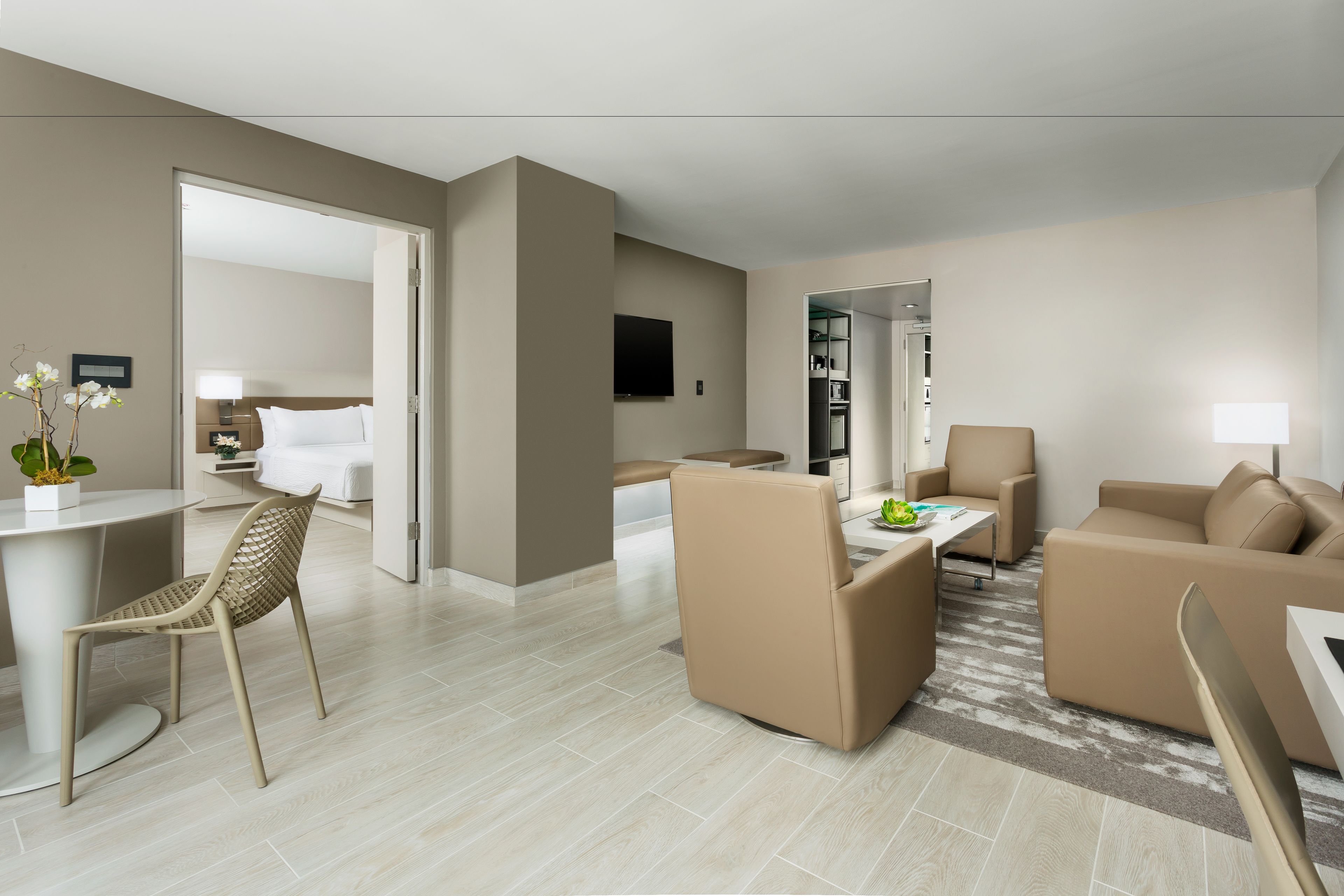 A modern hotel room with a living area, a dining table, a sofa, a chair, and a TV.