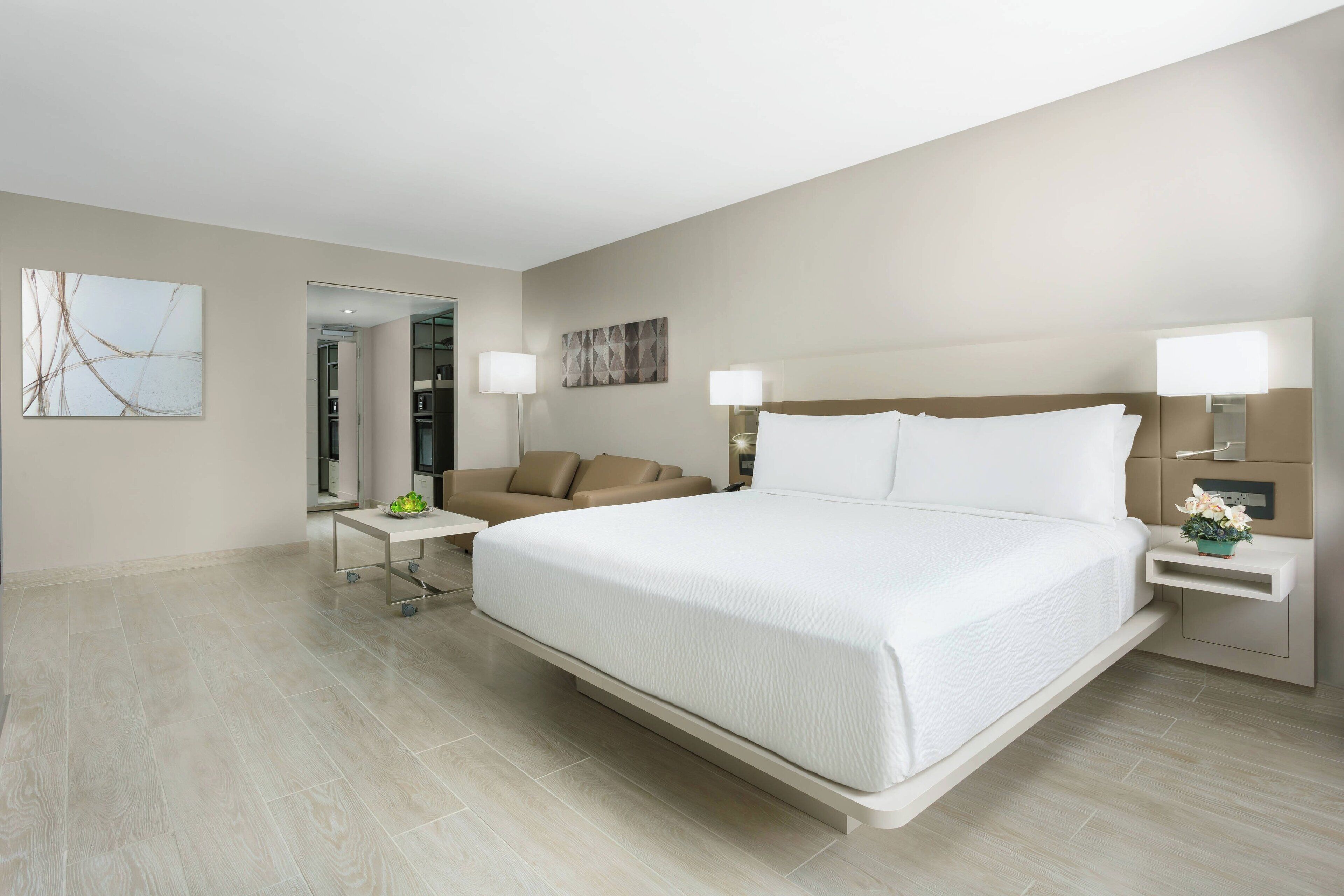 Una habitación de hotel moderna con una cama grande, una mesita de noche, un sillón y una pequeña mesa con una lámpara.