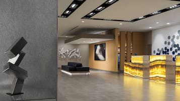Una zona de recepción moderna con una escultura geométrica, un sofá negro y un mostrador de recepción con paneles iluminados.
