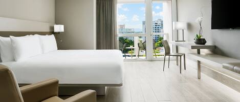 A modern hotel room with a large bed, a desk, a chair, and a TV mounted on the wall.