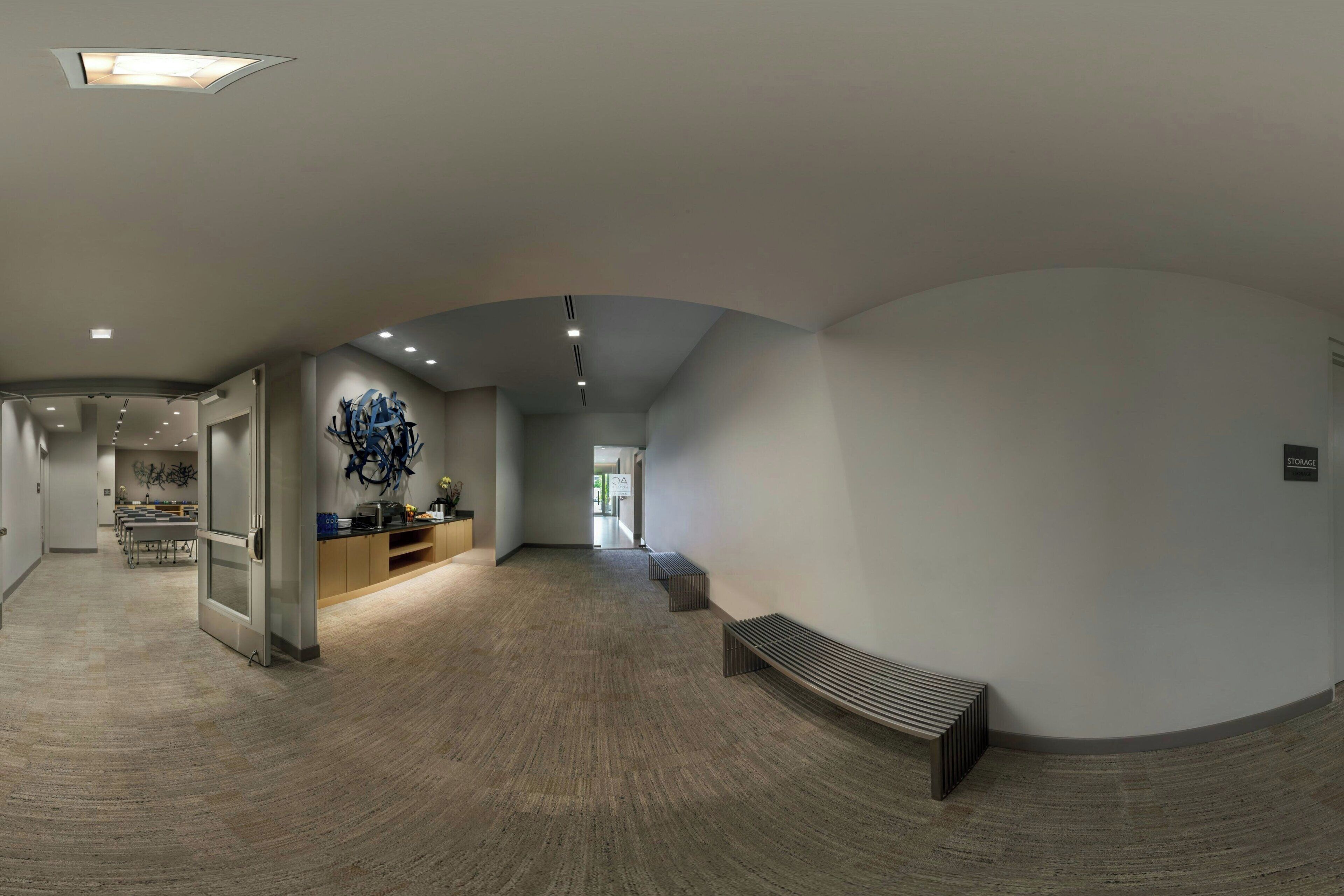 Un pasillo amplio con techo abovedado, una zona de recepción con mostrador moderno y obras de arte, y un espacio de estar con un banco.