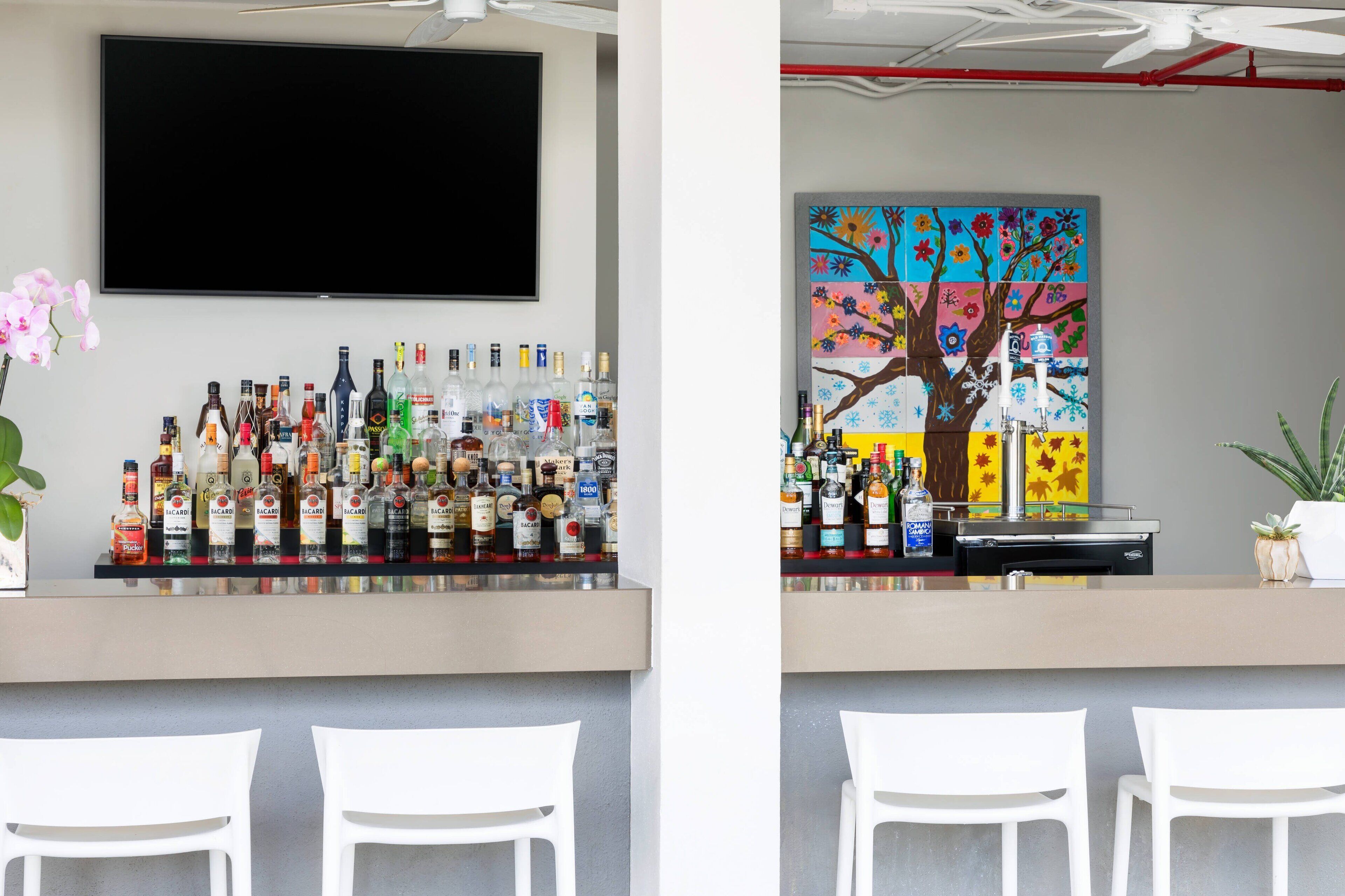 A bar area with a variety of liquor bottles, a flat-screen TV, and a colorful painting on the wall.