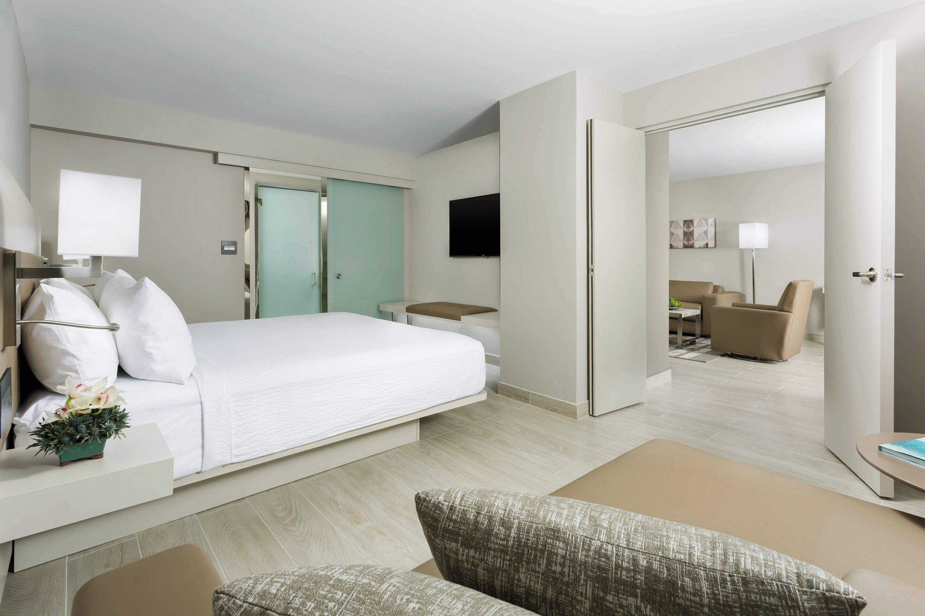 Une chambre d’hôtel moderne équipée d’un lit, d’un bureau, d’une chaise, d’une télévision et d’une porte donnant sur une autre pièce.