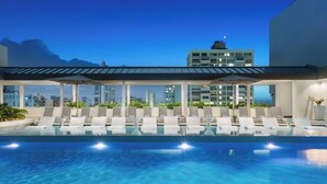 Una piscina en la azotea con sillones de descanso y vistas del horizonte de la ciudad.