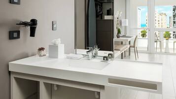Un baño moderno con un espejo grande, lavamanos blanco y vistas de la ciudad a través de la puerta de cristal.