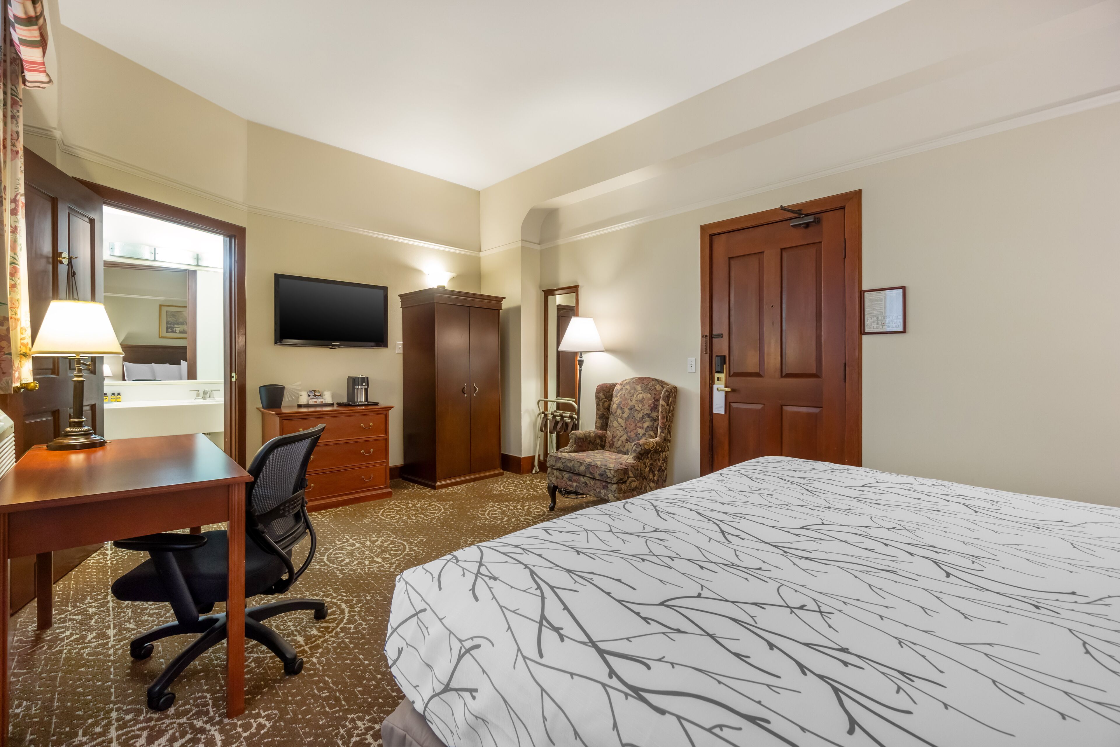 Une chambre d’hôtel comprenant un lit, un bureau, une chaise, une armoire, une télévision et une porte.