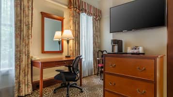 Habitación de hotel con un escritorio de madera, una silla, un aparador, un televisor, una lámpara y una cafetera.
