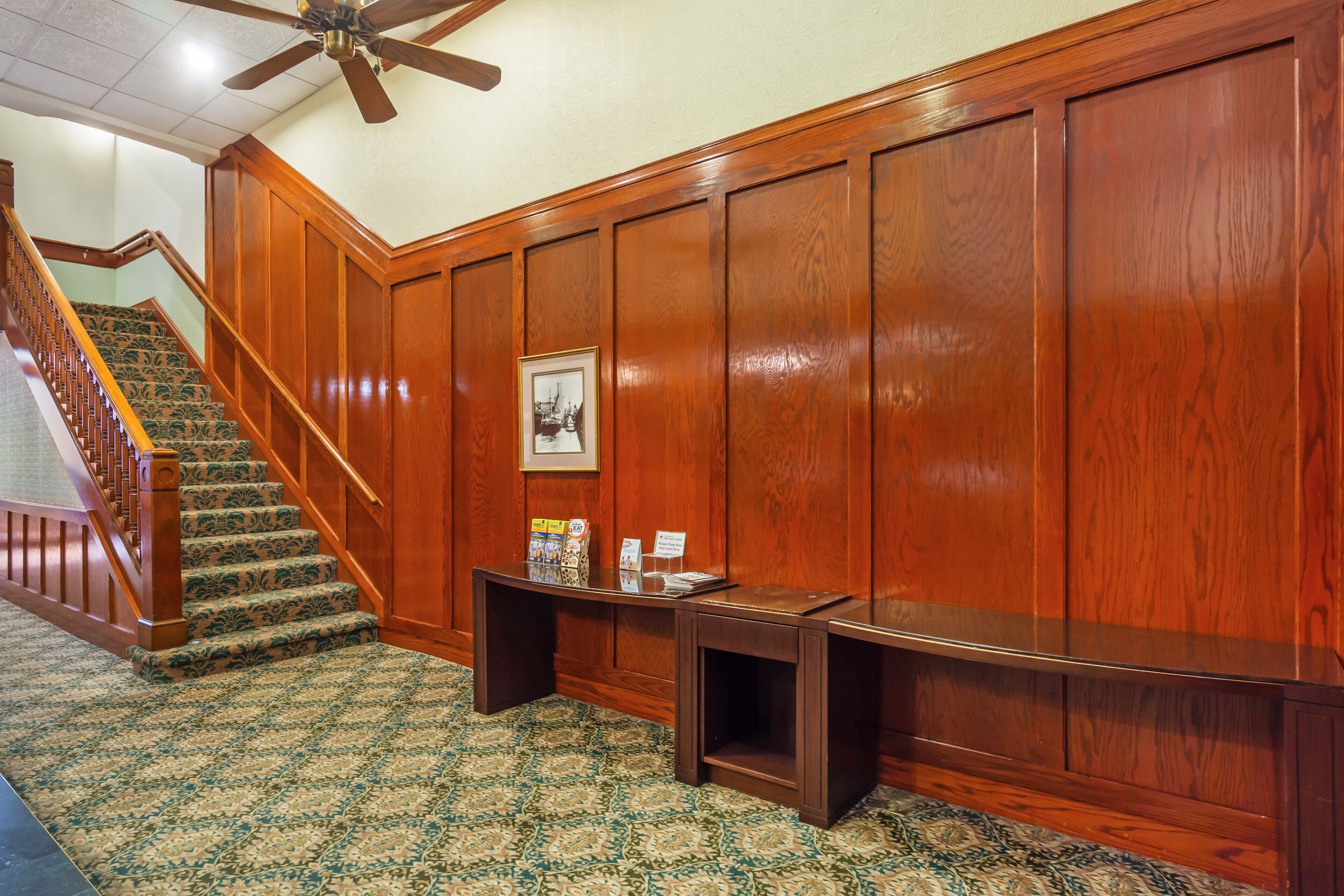 Un couloir aux murs lambrissés, un escalier recouvert de moquette et une petite table sur laquelle sont posés des magazines.