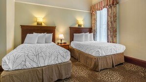 Dos camas dobles con cabeceras y pies de cama a juego, una mesita de noche con lámpara y una ventana con cortinas florales.