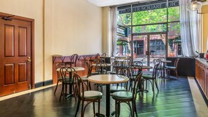 Interior acogedor de un restaurante con suelos de madera, mesas redondas y sillas de metal. Un amplio ventanal ofrece vistas a la calle.