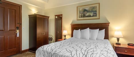 A hotel room with a large bed, two bedside tables with lamps, a wooden wardrobe, and a painting on the wall.