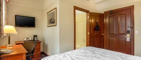 A hotel room with a bed, desk, chair, television, and a door leading to a bathroom.