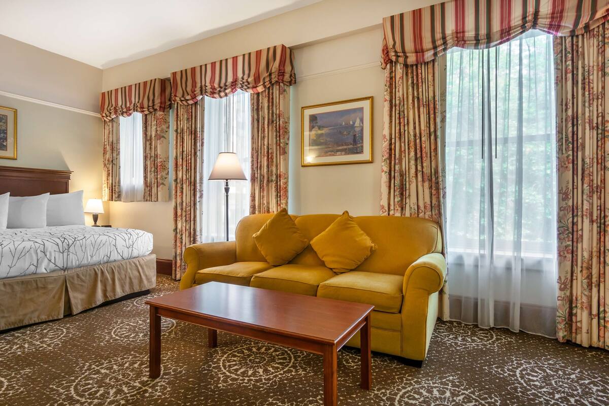 Una habitación de hotel con cama, sofá, mesa de centro y cortinas.