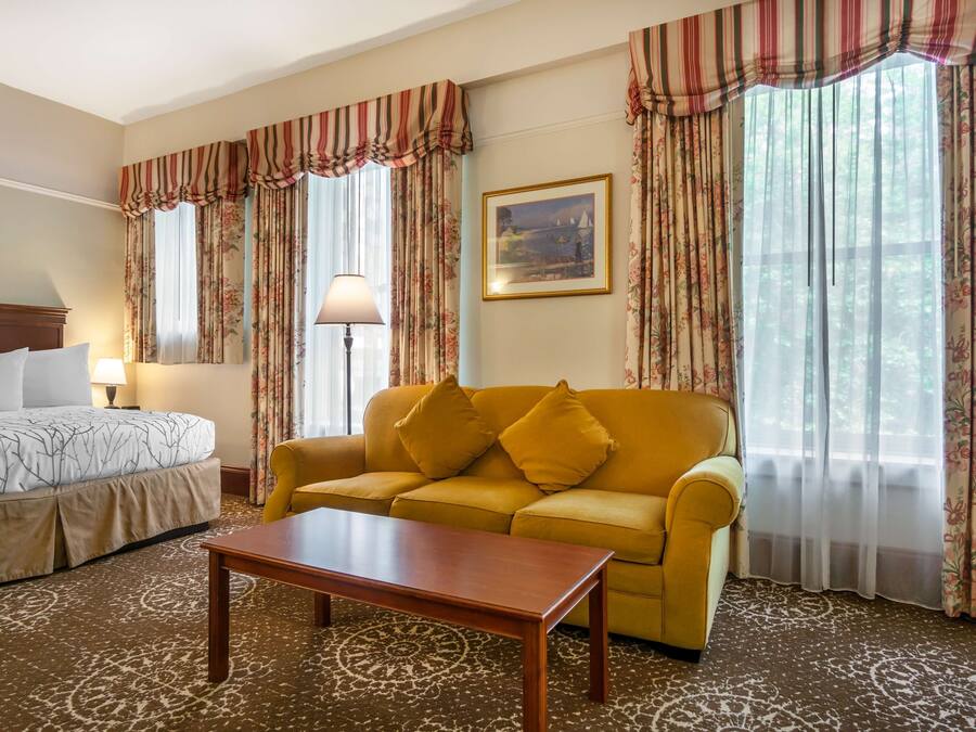 A hotel room with a bed, a sofa, a coffee table, and curtains.