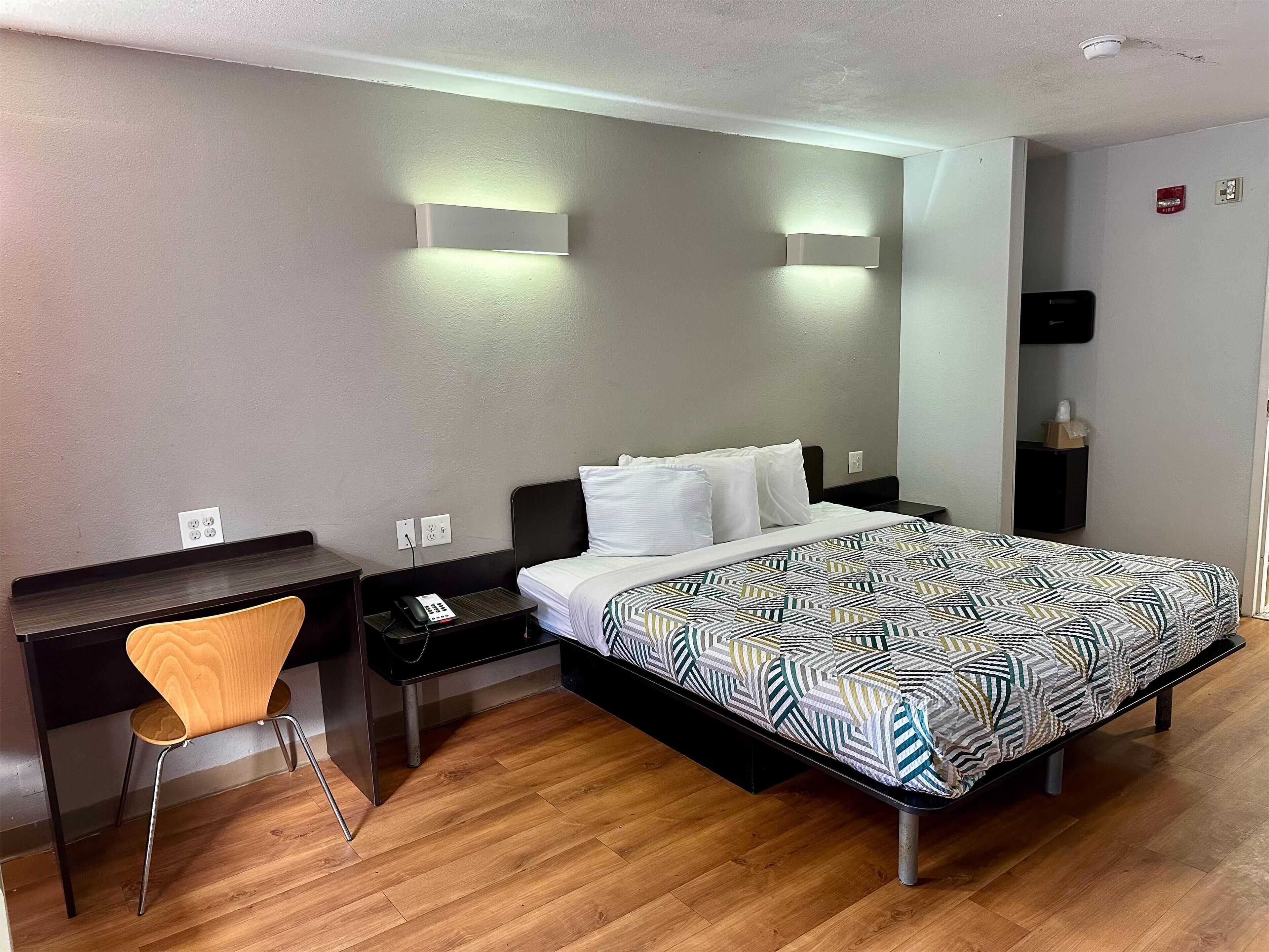 A hotel room with a bed, a desk, a chair, and a nightstand.