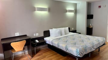 Quarto de hotel com uma cama, escrivaninha, cadeira e mesa de cabeceira.