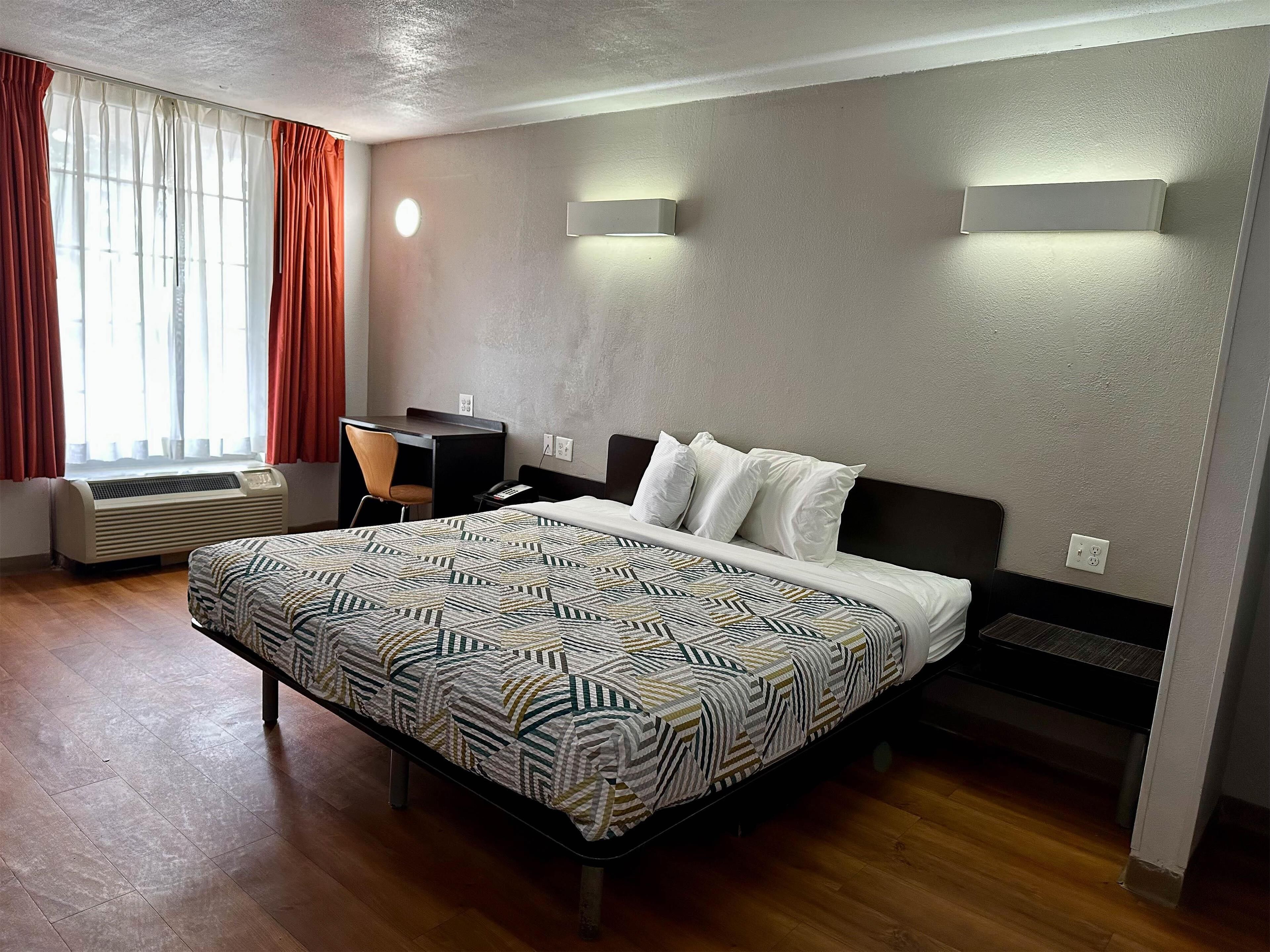 A hotel room with a bed, a desk, a chair, and a window with curtains.