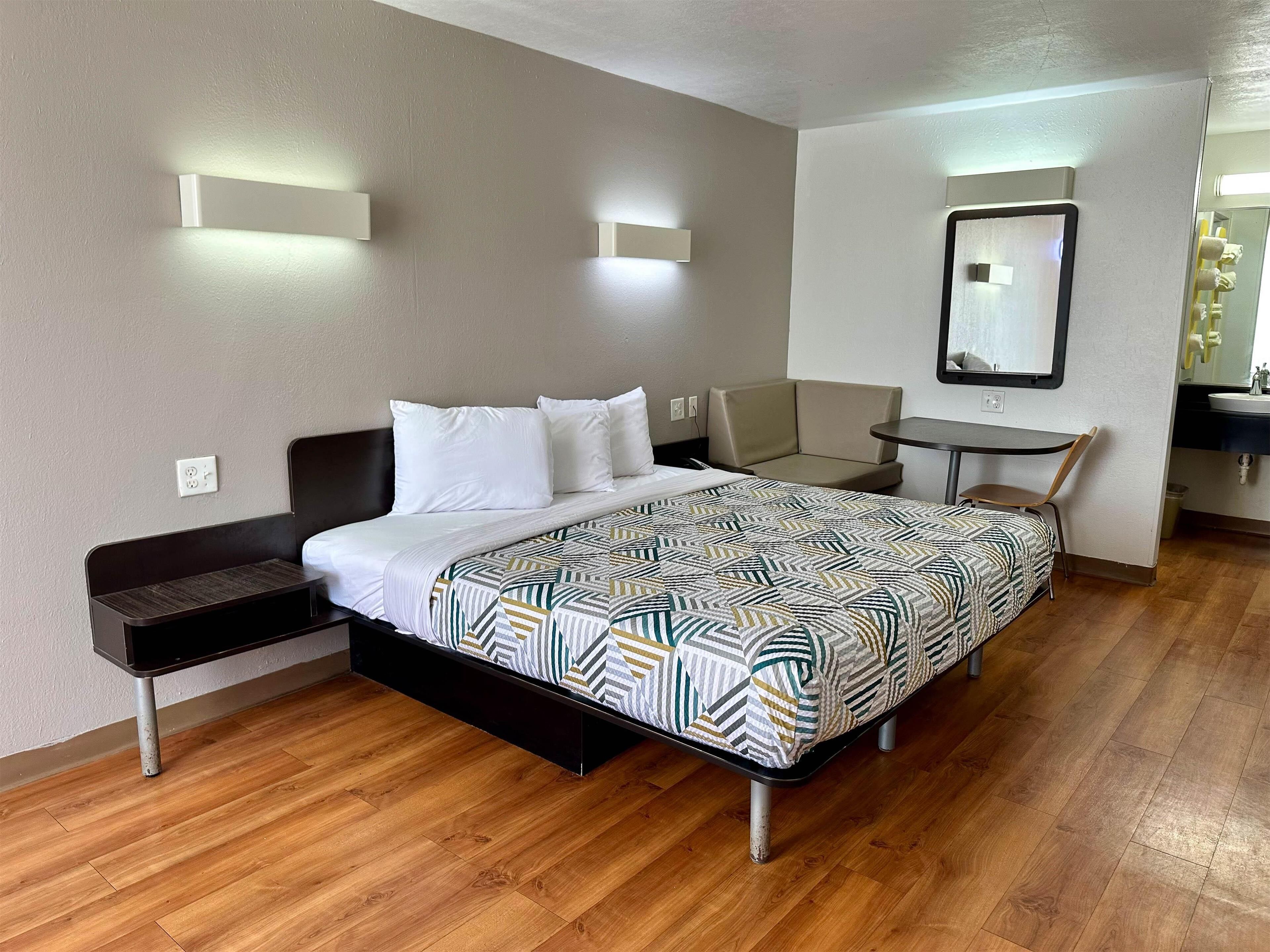 A hotel room with a bed, a small table, a chair, and a mirror.