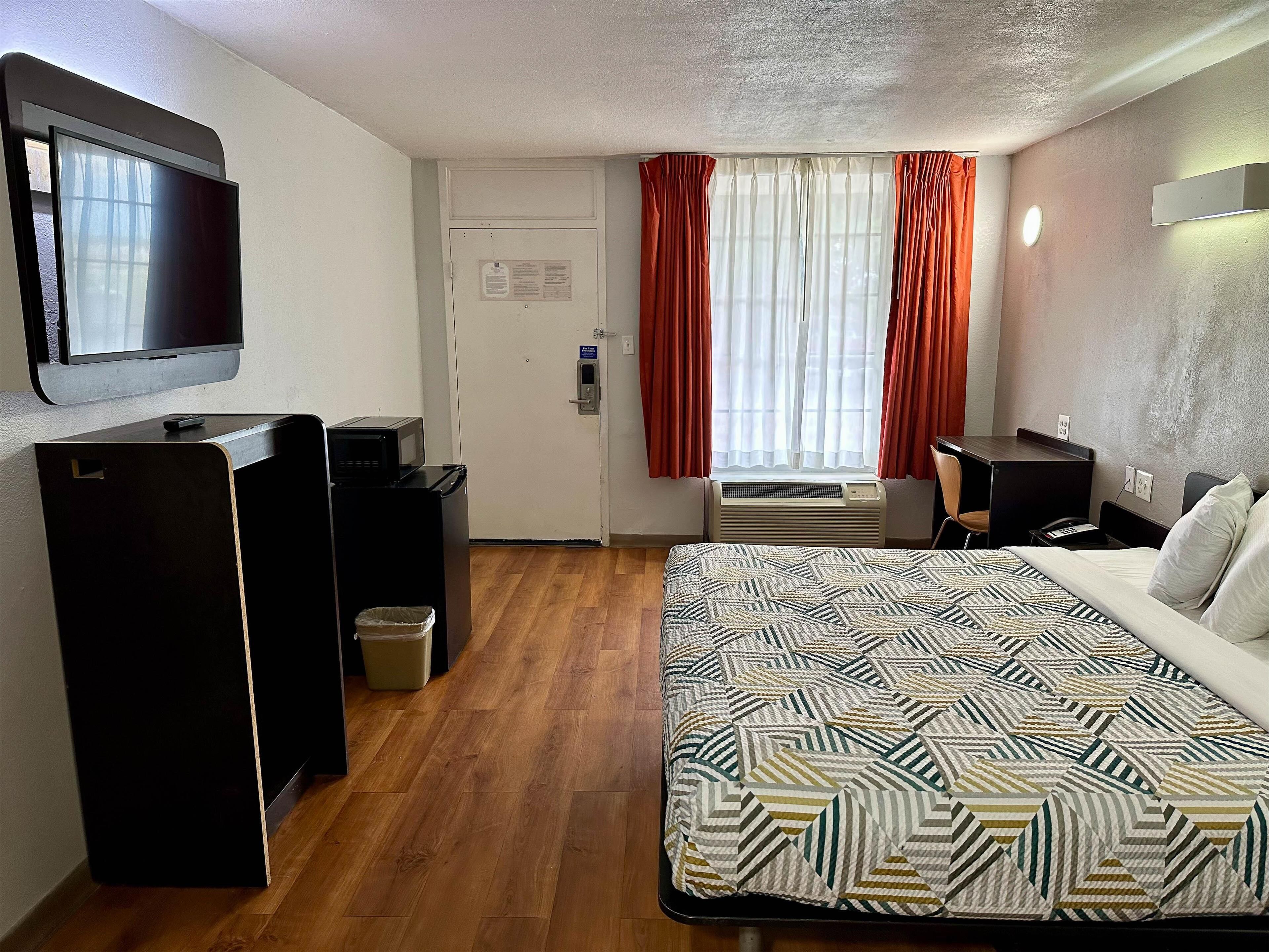Una habitación de hotel con cama, escritorio, televisión, microondas y cubo de basura.