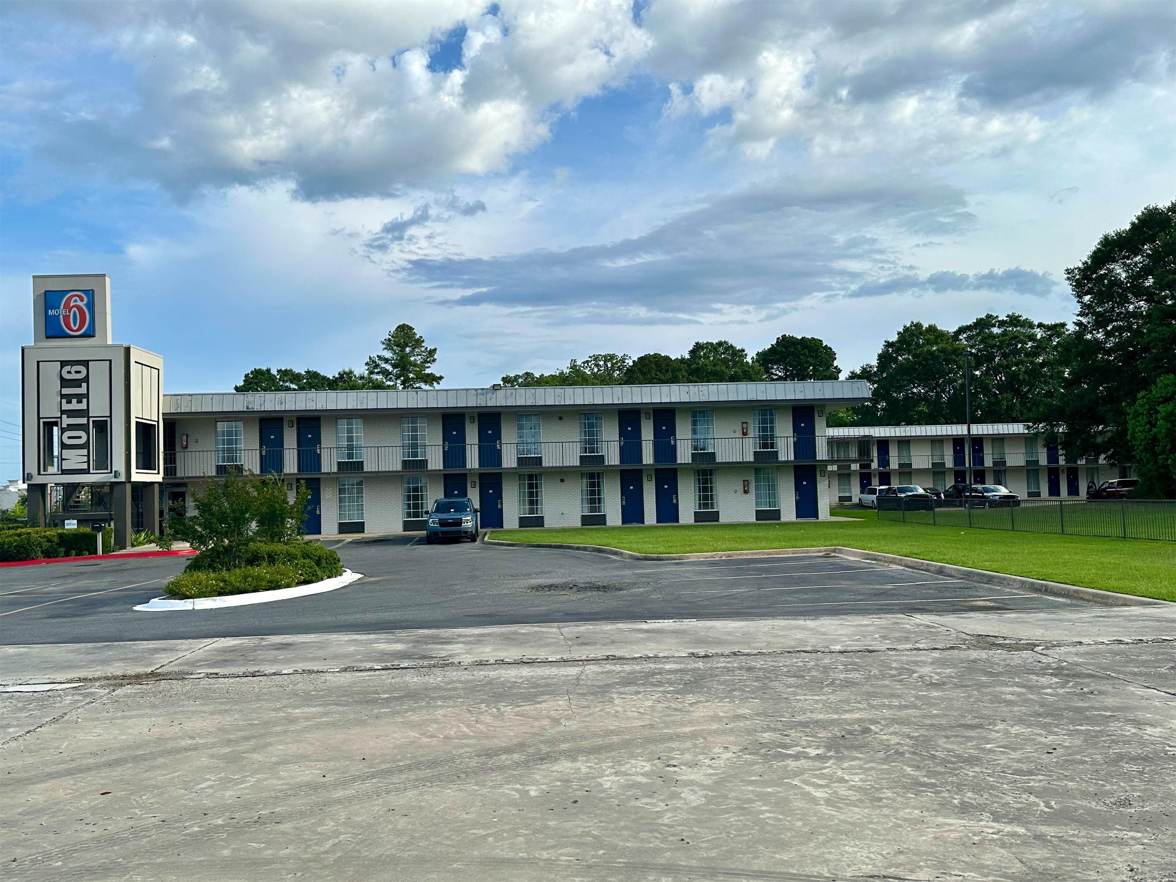 A motel with a central parking lot, multiple units with blue doors, and a sign indicating the motel name.