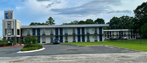 A motel with a central parking lot, multiple units with blue doors, and a sign indicating the motel name.
