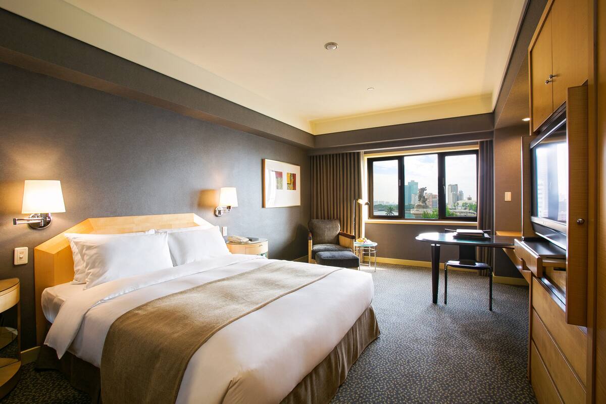 A hotel room with a large bed, a desk, a chair, and a TV.
