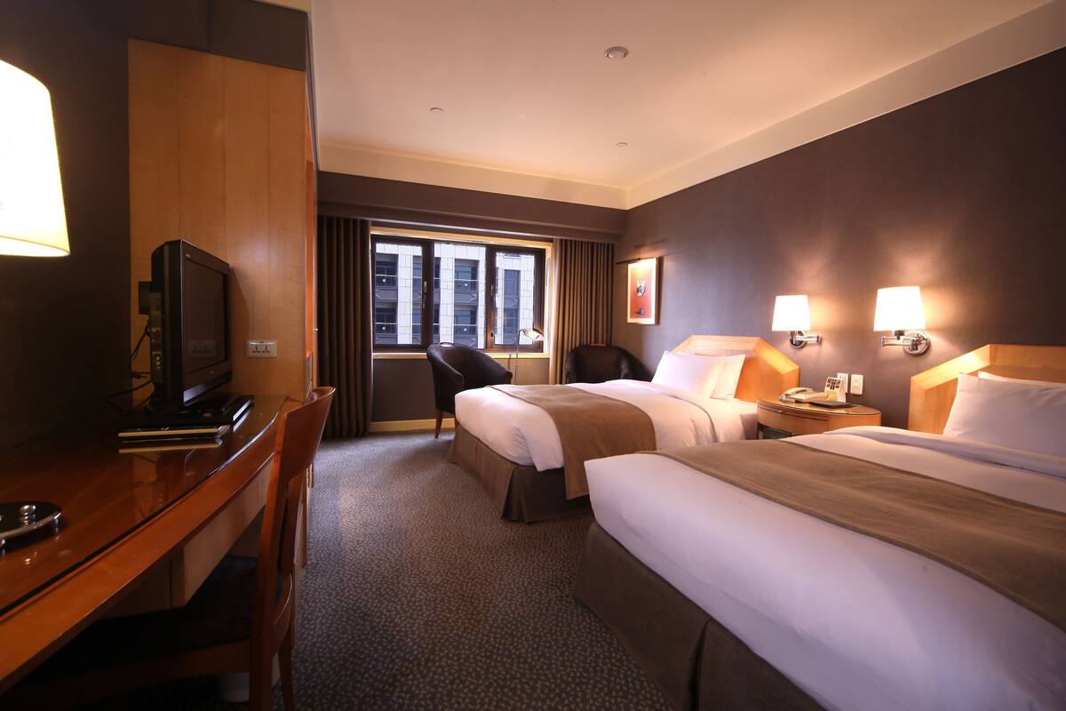 A hotel room with two beds, a desk with a television, and a chair.