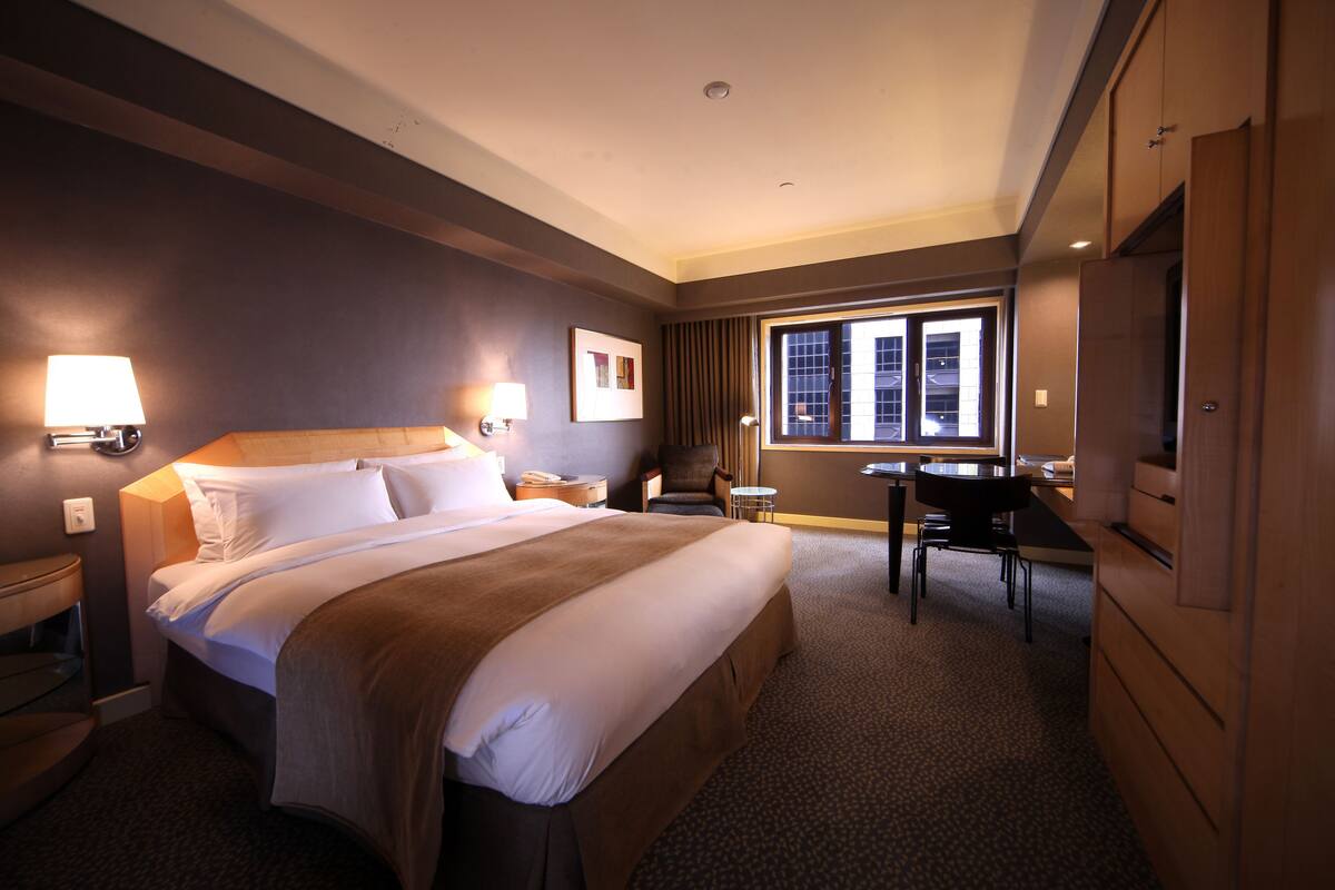 A hotel room with a large bed, a desk, a chair, and a TV.