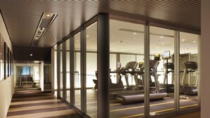 Une salle de sport moderne avec des murs en verre, des tapis de course et des vélos d’appartement.