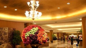 Un hall d’entrée agrémenté d’un grand arrangement floral sur une table, d’un lustre et d’un sol à carreaux.