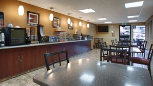 A restaurant with a counter, chairs, tables, and a television screen.