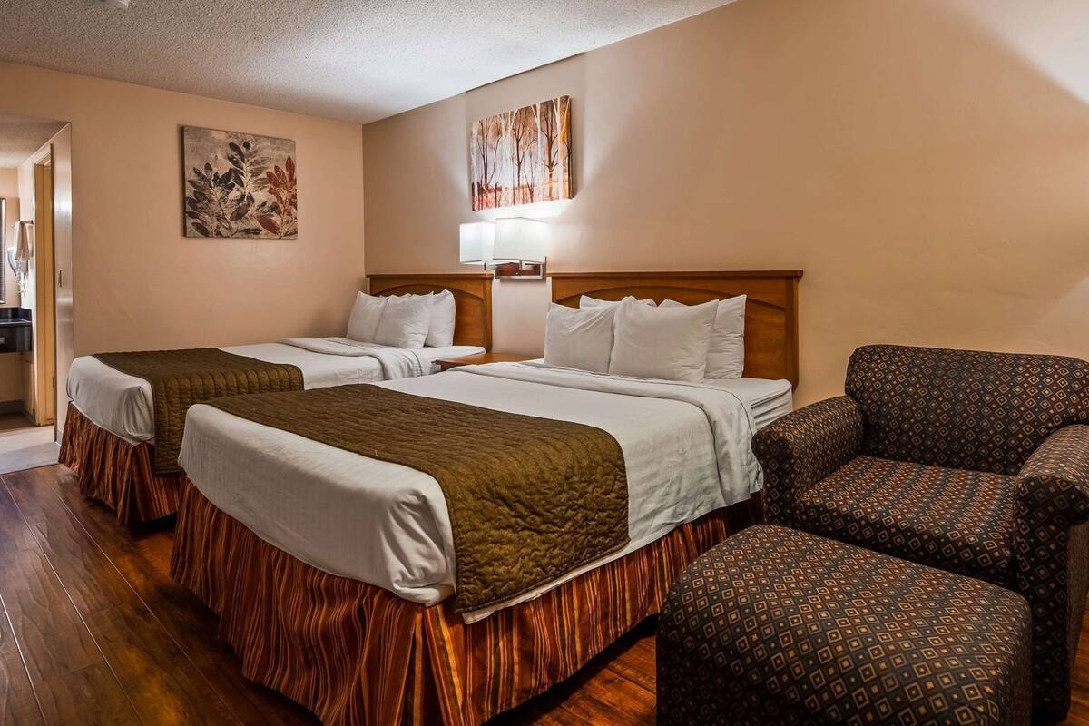 A hotel room with two beds, a patterned armchair, and artwork on the walls.