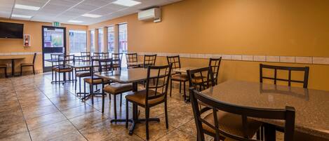 A restaurant with multiple tables and chairs, a tiled floor, and an exit sign.