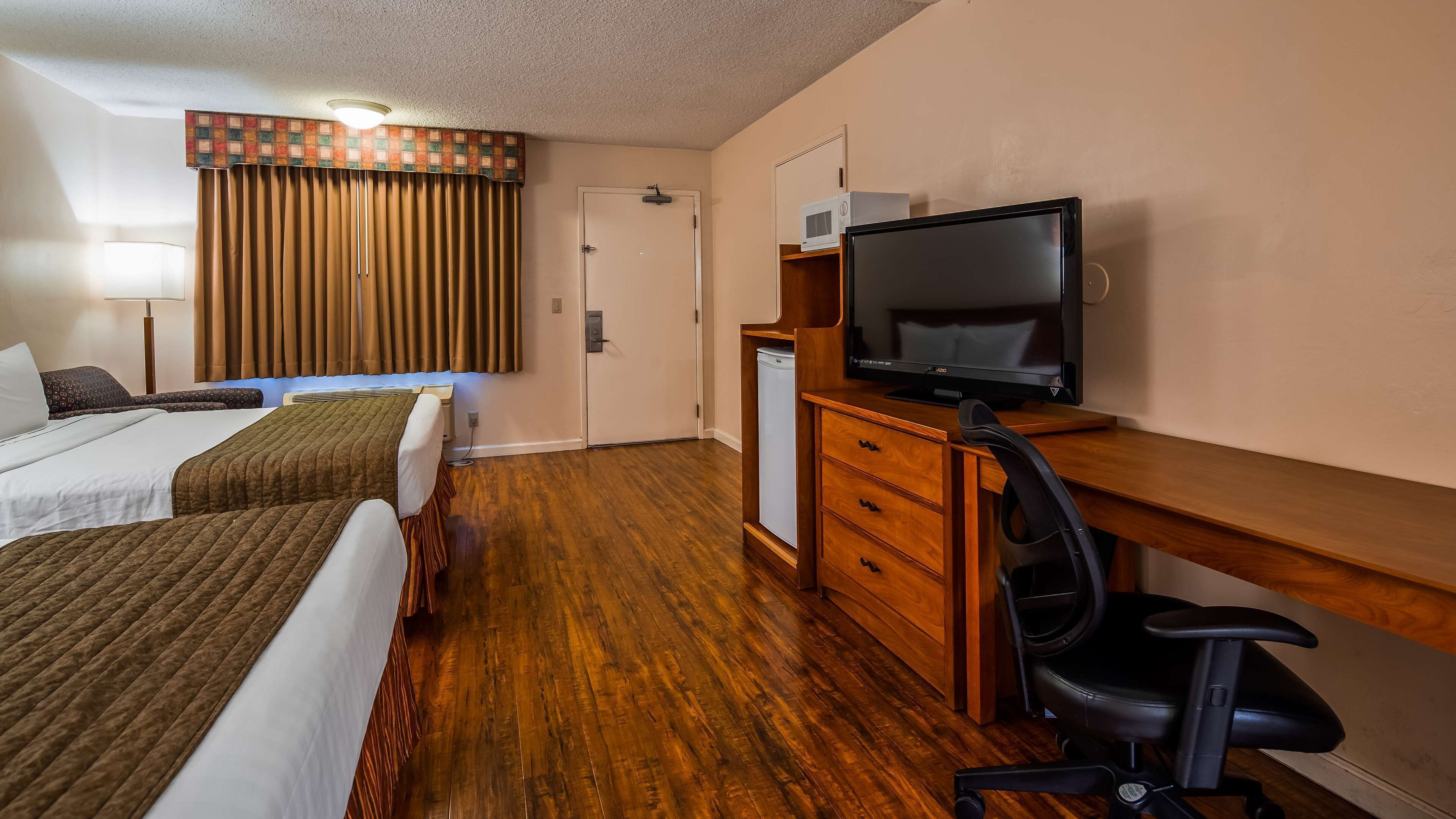 A hotel room with two beds, a desk with a TV, a chair, a wardrobe, and a small refrigerator.