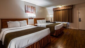 A hotel room with two beds, a painting on the wall, a window with curtains, and a door.