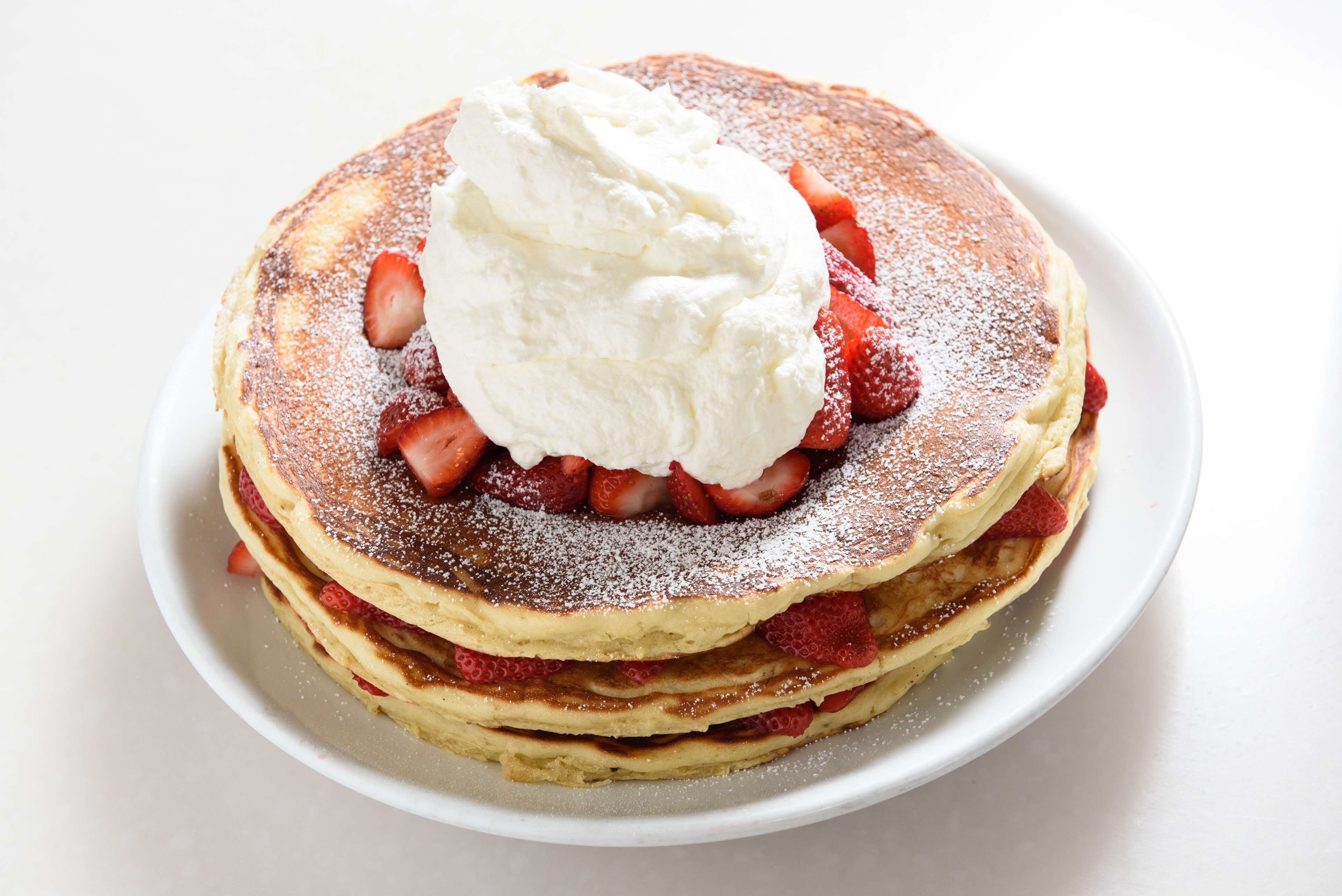 A stack of pancakes with whipped cream and strawberries on a white plate.