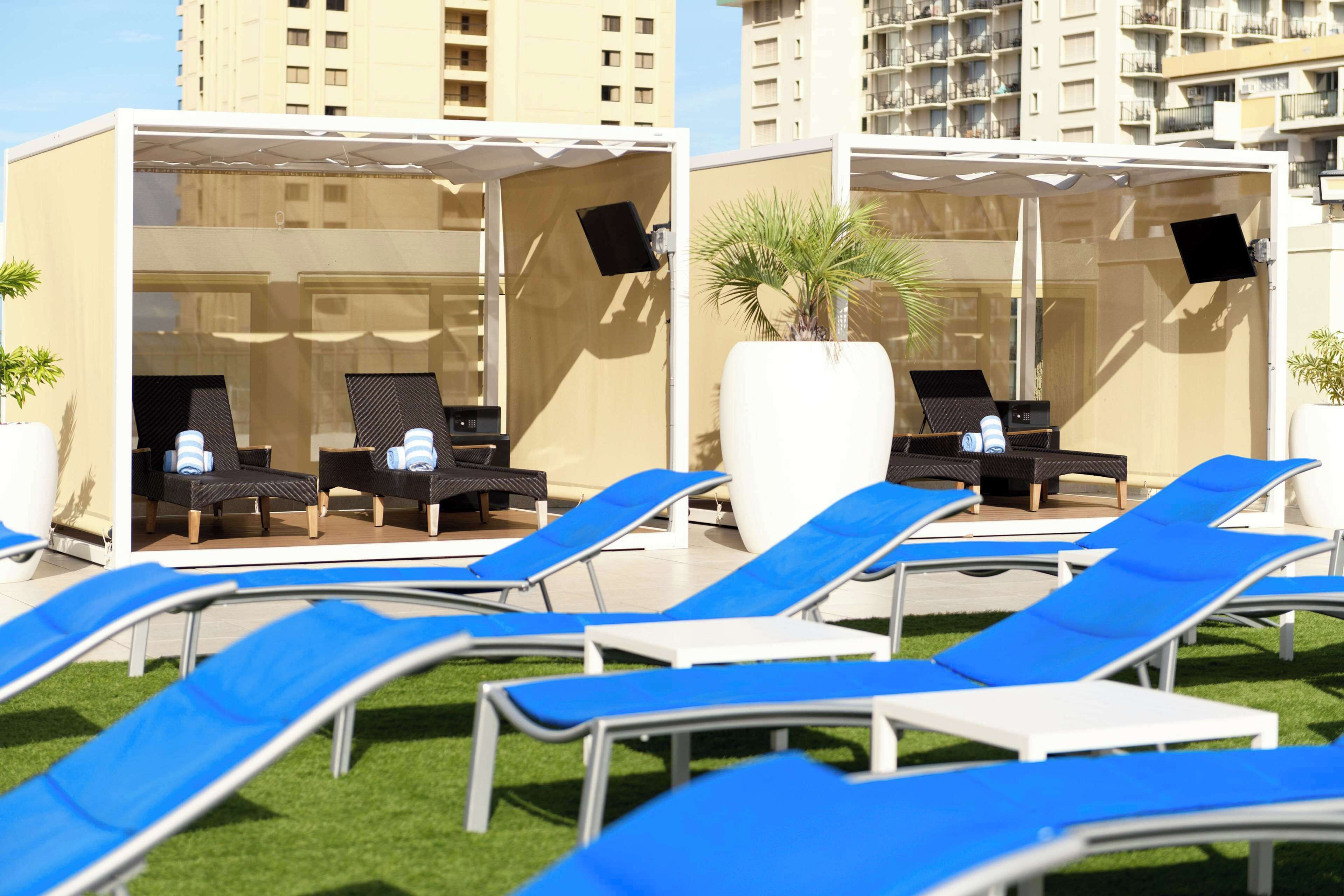 A rooftop lounge area with blue lounge chairs and a covered seating area with black chairs and a white table.