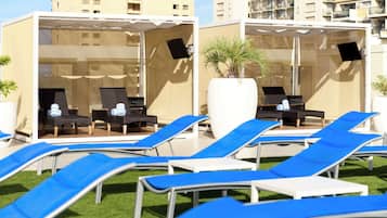 A rooftop lounge area with blue lounge chairs and a covered seating area with black chairs and a white table.