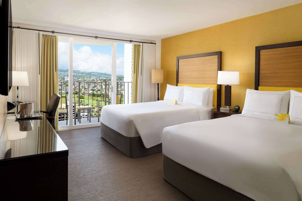 A hotel room with two beds, a desk, and a view of the city.