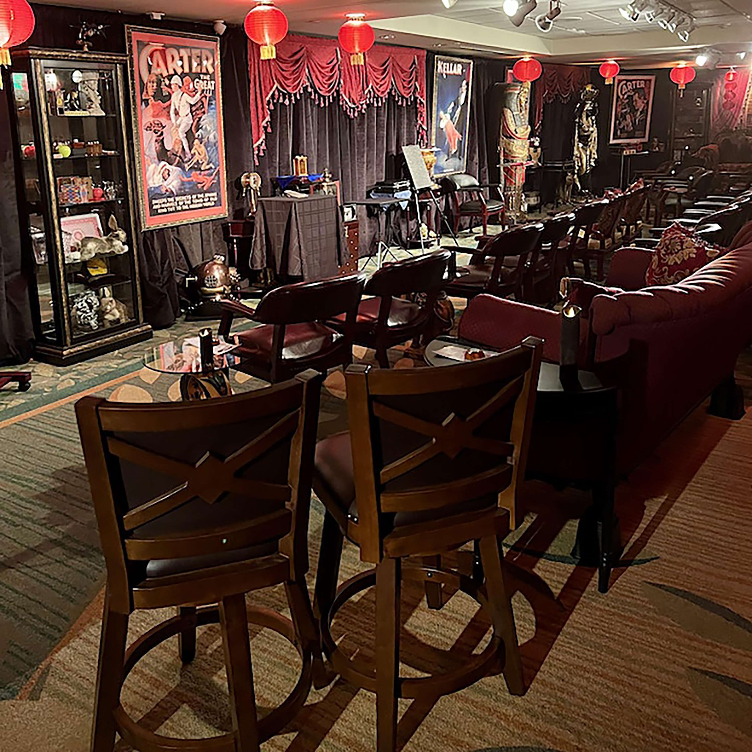 Une pièce faiblement éclairée, décorée dans un style rétro, avec notamment un canapé rouge, des chaises en bois et un vieux juke-box.
