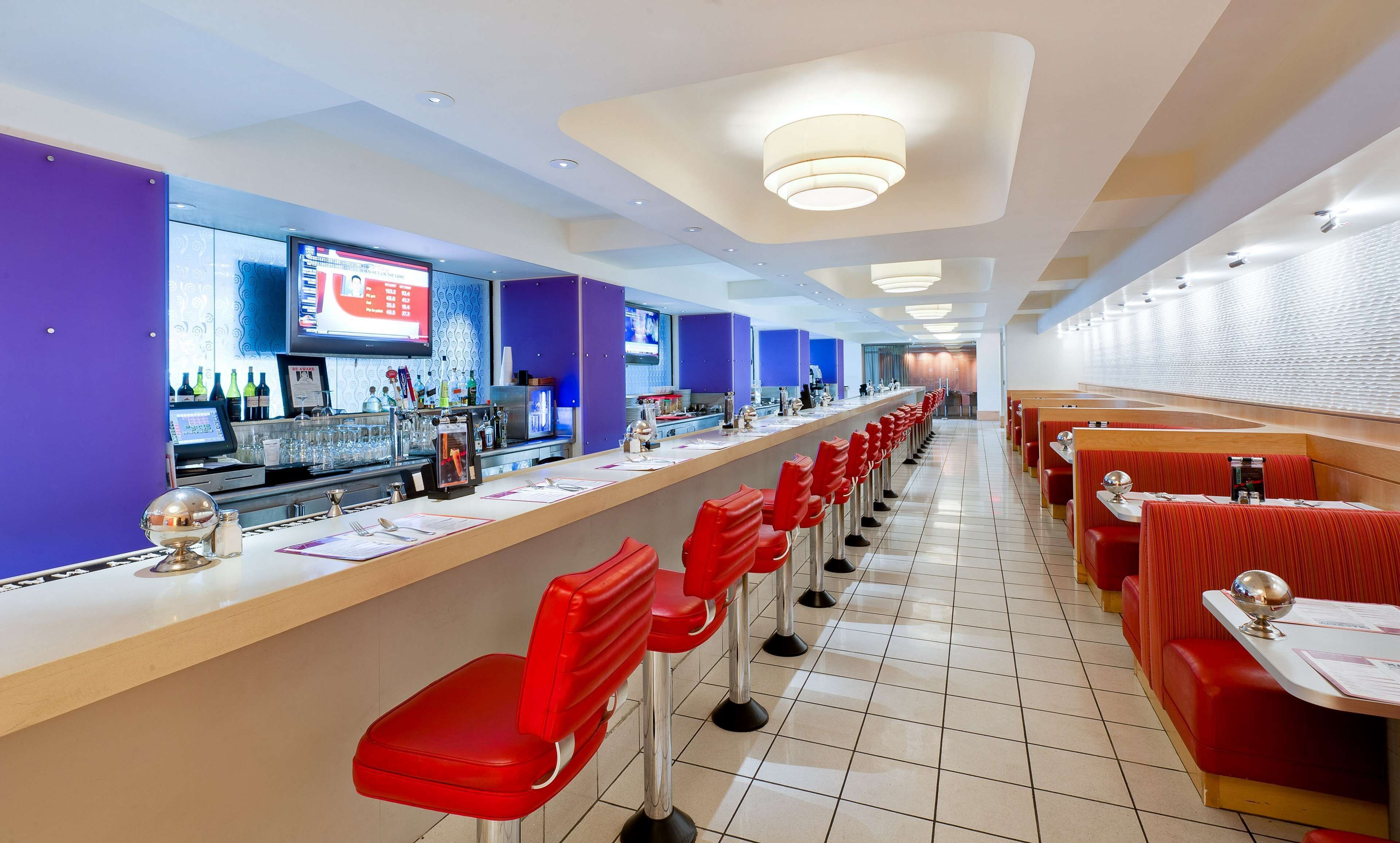 A restaurant with a long counter, red bar stools, and a modern interior design.