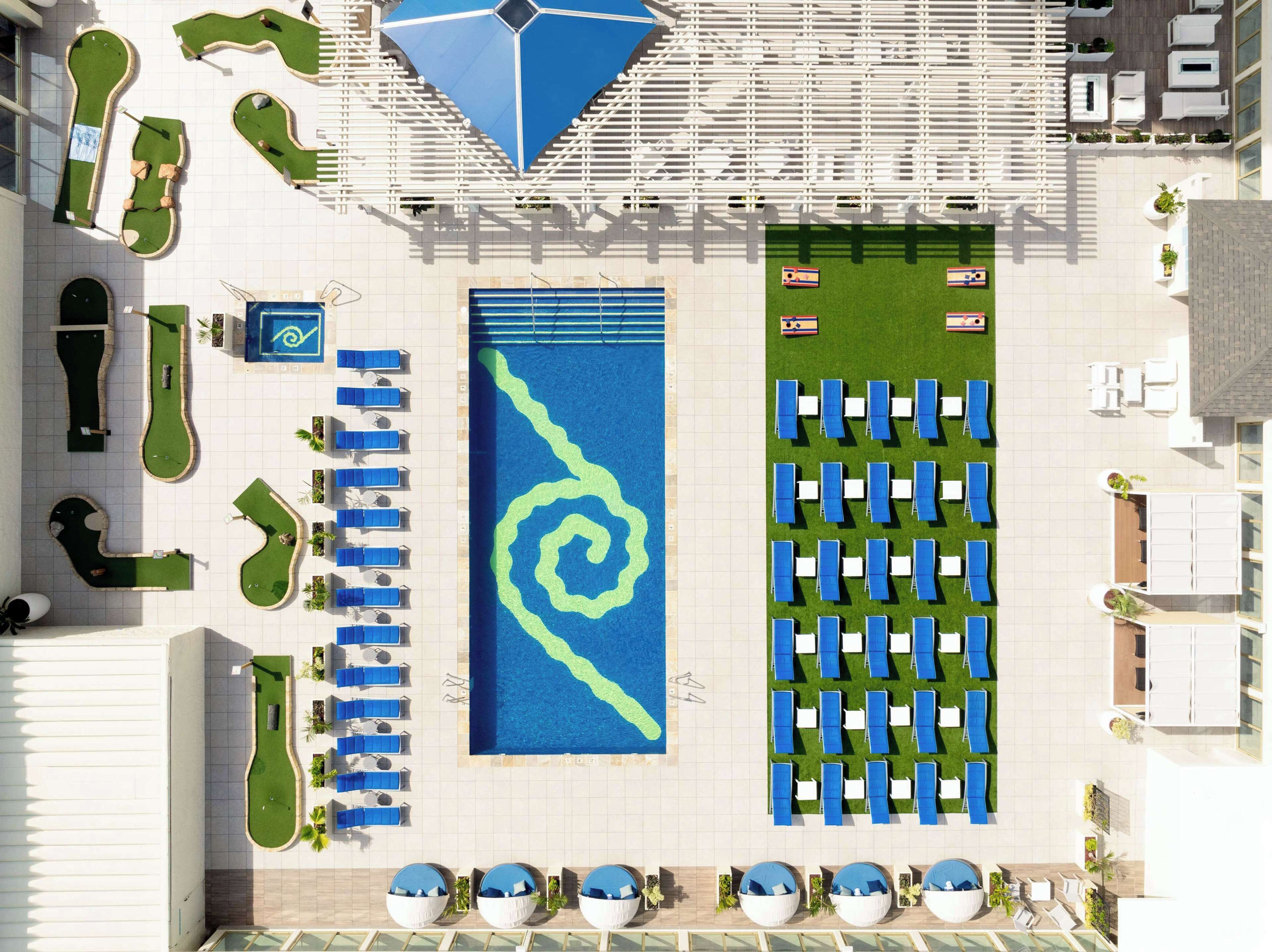 An aerial view of a hotel with a large swimming pool, multiple lounge areas, and a golf course.