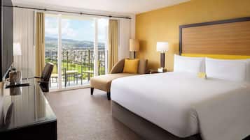 Habitación de hotel con una cama grande, un escritorio, una silla y vistas a un paisaje urbano a través de amplias ventanas.
